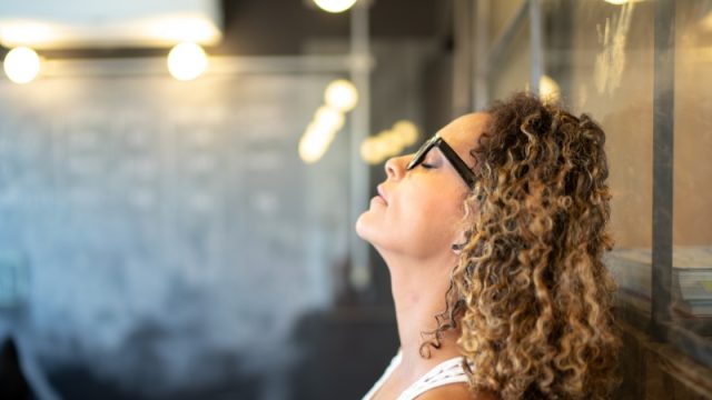 Young woman leaning head back in the wall, thinking with her eyes closed.