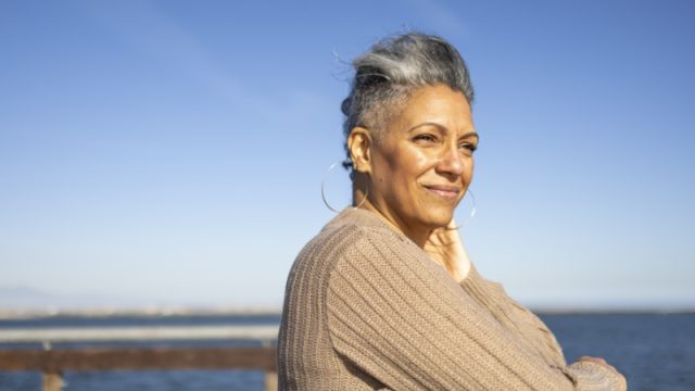 A mature black woman relaxes on the pier at the beach.