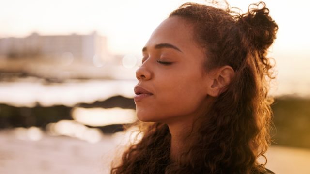 Young woman sitting alone on a mat and meditating on the beach at sunset