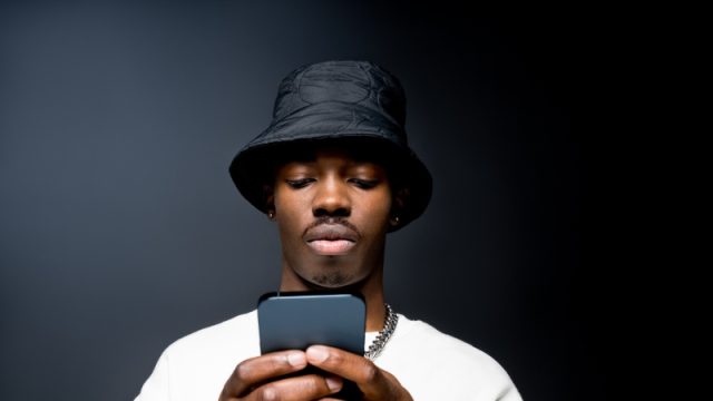 young man wearing white sweatshirt and black bucket hat, using mobile phone.