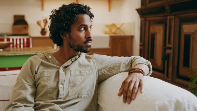 young man sitting alone on the sofa at home and looking contemplative